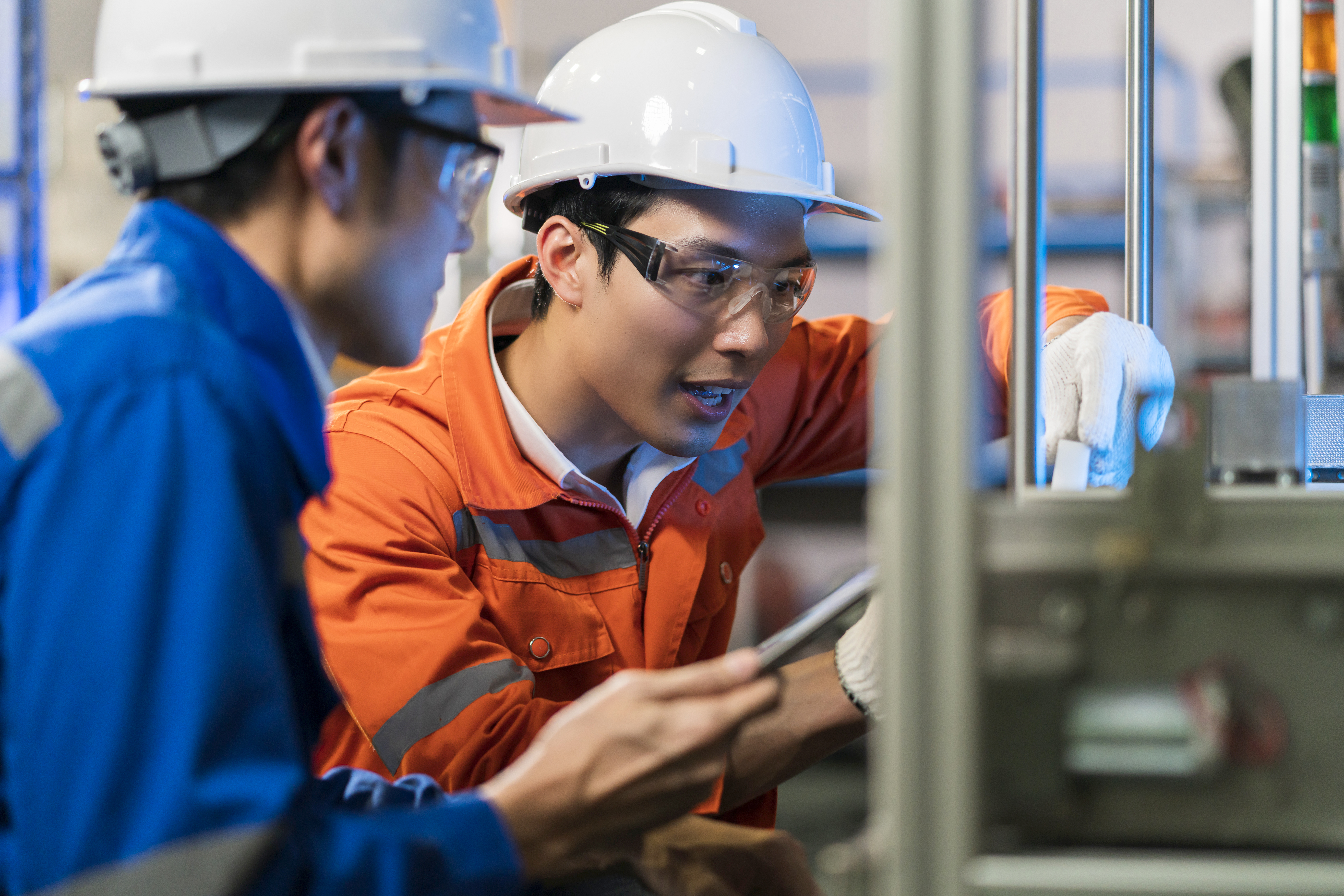 Two workers discussing and inspecting machinery in a factory setting. Two workers discussing and inspecting machinery in a factory setting.