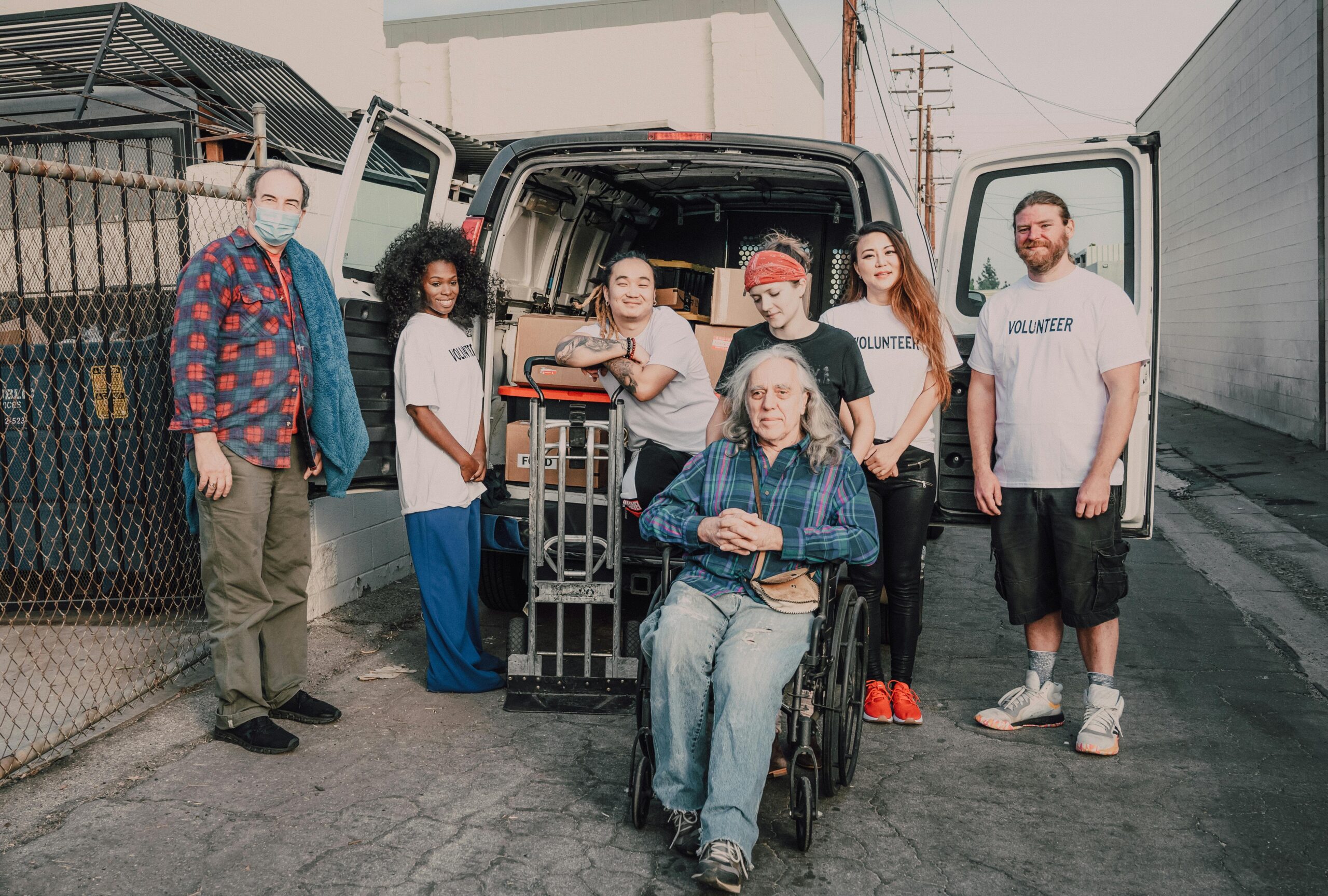 Volunteers stand beside delivery van with elderly person in wheelchair Volunteers stand beside delivery van with elderly person in wheelchair